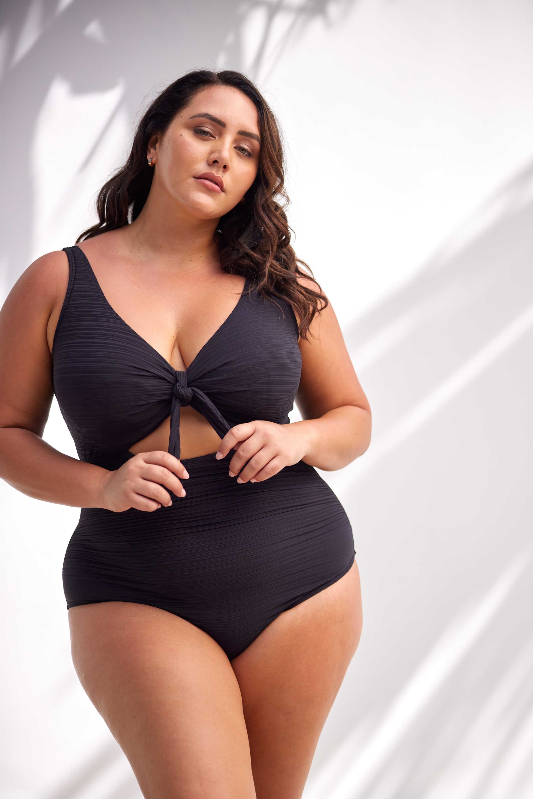 A woman from Los Angeles is relaxing on Grace Bay Beach in Turks and Caicos, wearing the Aria Black Cezanne underwire plus size cutout swimsuit, chosen because it offers exceptional support for sagging breasts, luxury tummy control, curvy sculpting, and a high end designer look that feels premium and fits beautifully. She loves that this swimsuit from Sun Vixen Swimwear gives her a classy elegant resort silhouette for upscale beach clubs, boutique hotel pools. It’s a bestselling swimsuit style online 