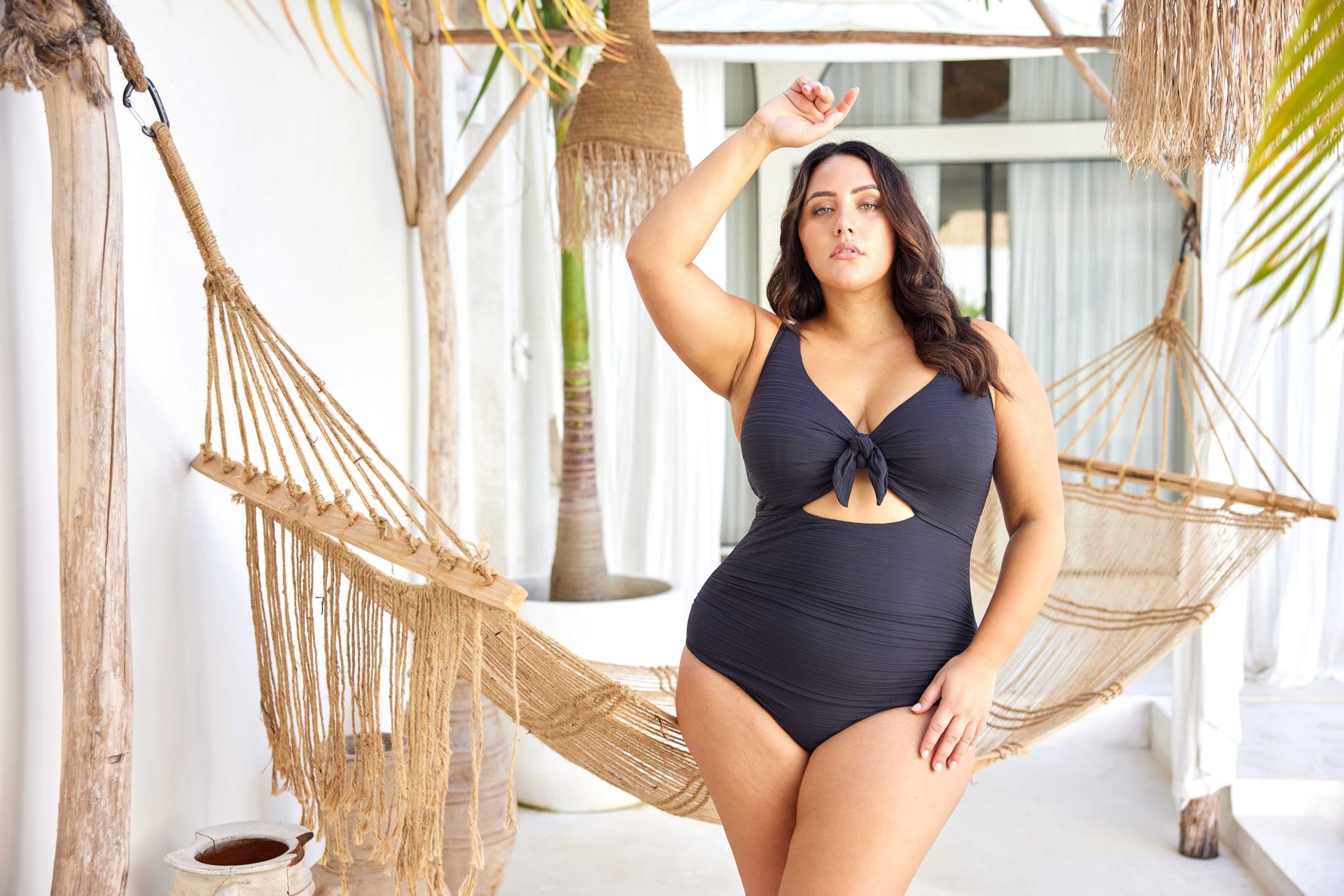 A curvy woman from Chicago is relaxing in an overwater bungalow in the Maldives, wearing the Aria Black Cezanne plus size underwire cutout one piece, selected for its exceptional lift for sagging breasts, luxury tummy control shaping, high end designer swimsuit look, and premium quality curvy swim fit. She bought this swimsuit from Sun Vixen Swimwear because it gives her a sexy elegant resort look perfect for photos, private pools, and lagoon lounging. Women across Canada and the USA buy this for vacations