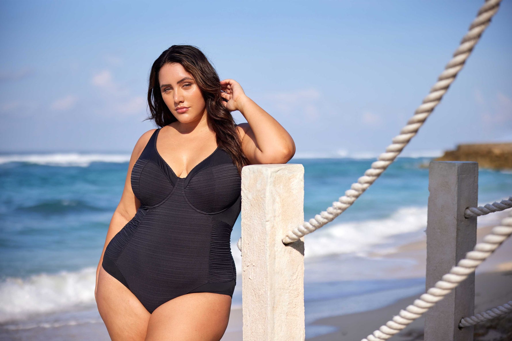 A curvy woman from Montreal is relaxing on the beaches of Playa del Carmen, Mexico, wearing the Plus Size Aria Giotta Artesands luxury underwire swimsuit, chosen for its premium tummy control, curvy sculpting features, supportive lift for sagging breasts, and high end designer swimsuit style that matches the look of her luxury resort. Travelers from Vancouver, New York City, Dallas, Edmonton, Canada USA buy this swimsuit for vacations in Turks and Caicos, Barbados, Maldives for luxury plus size resort swim