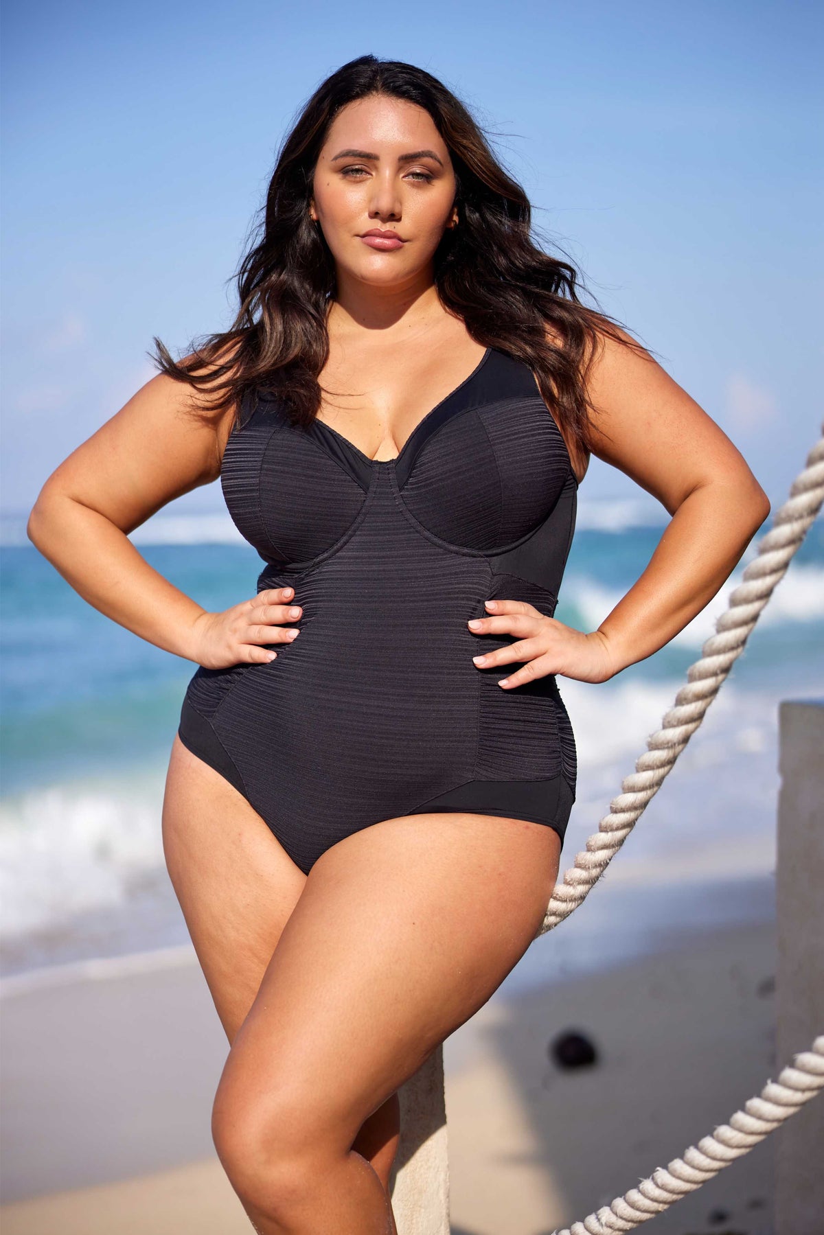 A curvy woman from Toronto is spending a luxury week in the Maldives, walking across white sand and heading toward her overwater villa while wearing the Plus Size Aria Giotta Artesands luxury underwire swimsuit, a premium one piece swimsuit for women wanting supportive lift for sagging breasts, high quality tummy control shaping, and curvy sculpting swimwear that feels elegant and expensive for upscale resort travel. She chose this premium plus size bathing suit it gives her a sleek classy slimmed look 