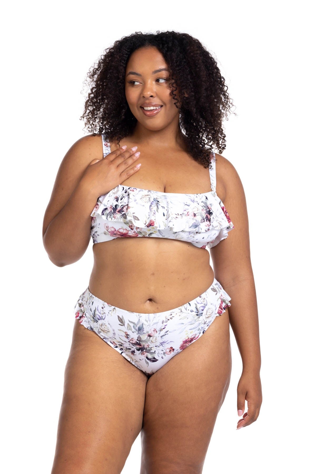 A curvy woman from Orlando Florida is wearing the Clementine White Vermeer Artesands flounce bikini with its pretty ruffle details, slimming silhouette, and supportive high waist tummy control bikini bottoms. She ordered it from Sun Vixen Swimwear USA, her go to for luxury shapewear swimwear, classy chic plus size bikinis, and best tummy control bikinis for moms. She loves how the floral bikini makes her look sophisticated. The strong compression fit helps her feel confident and slim throughout her trip