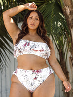A plus size woman from San Diego California is wearing the Clementine White Vermeer flounce bikini by Artesands, a cute floral swimsuit with a frilly ruffle bikini top and high waist supportive tummy control bottoms that give a slimming shapewear feel. She bought it from Sun Vixen Swimwear USA Canada because she loves sexy plus size designer swimwear and the most flattering bikinis for plus size women online, especially pretty white floral swimwear for moms who want confidence and a luxury beach aesthetic
