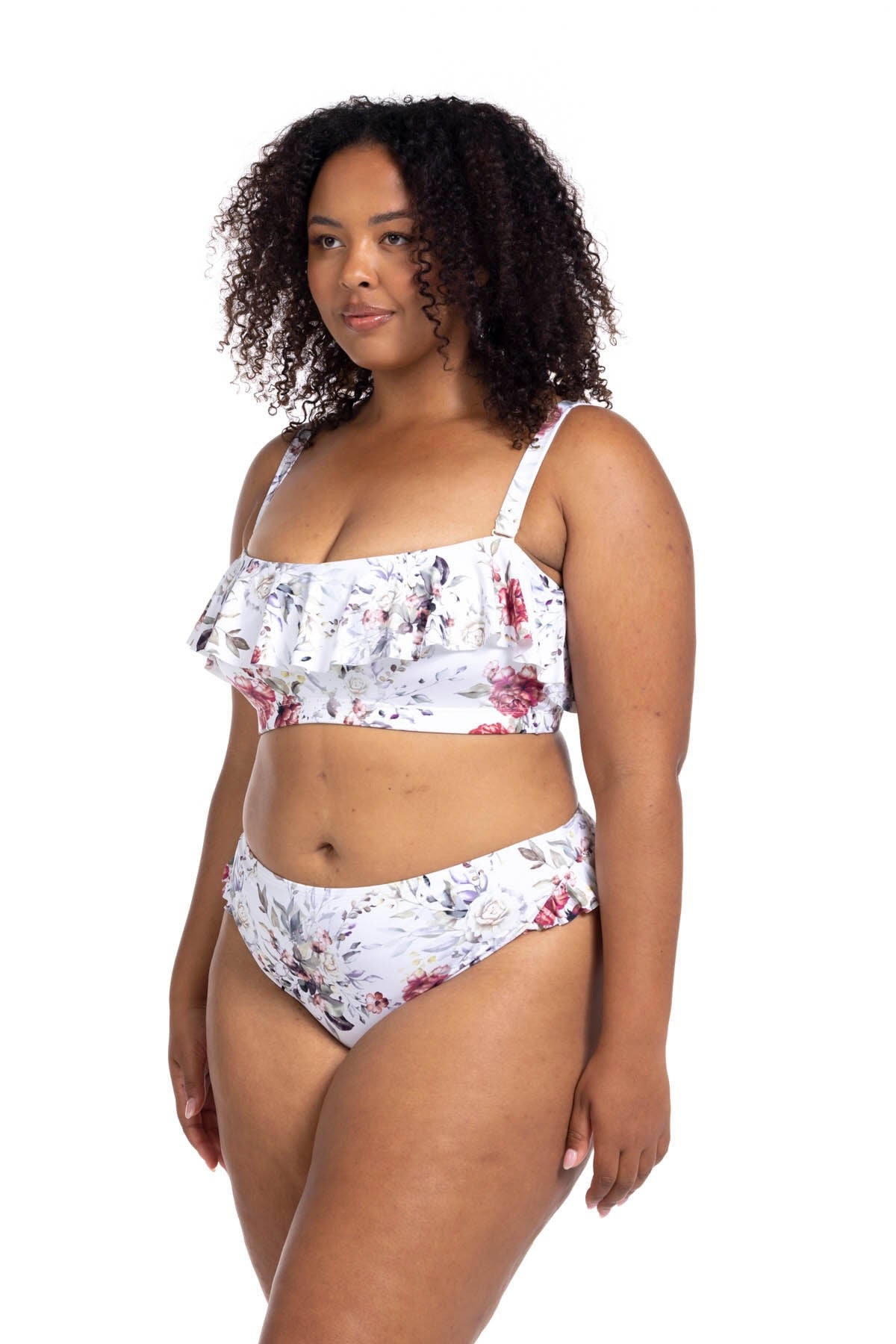 A plus size woman from New Jersey is wearing the Artesands Clementine White Vermeer frilly bikini during her beach weekend, loving the floral ruffle aesthetic and high waist tummy control bottoms that smooth and sculpt her curves. She chose Sun Vixen Swimwear because it offers the best plus size swimwear in USA and Canada and cute sexy plus swimsuits for women who want a polished luxury look. She appreciates how the floral bikini looks classy and elegant. The compression waistline keeps her silhouette slim
