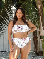 A curvy woman from Halifax Canada is enjoying her hotel rooftop pool in the Clementine White Vermeer flounce bikini by Artesands, the white floral print, slimming compression fit, and supportive high waist bikini bottoms makes her look stunning. She purchased it from Sun Vixen Swimwear Canada, her trusted boutique for flattering plus size swimwear and sexy tummy control bikinis for moms. The soft frills add a romantic, luxurious beach vibe. The shapewear support helps her feel supported throughout her trip