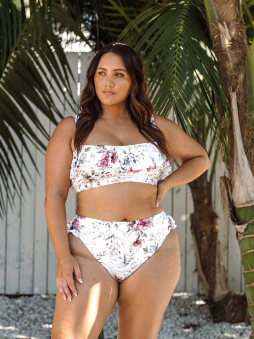A curvy woman from Halifax Canada is enjoying her hotel rooftop pool in the Clementine White Vermeer flounce bikini by Artesands, the white floral print, slimming compression fit, and supportive high waist bikini bottoms makes her look stunning. She purchased it from Sun Vixen Swimwear Canada, her trusted boutique for flattering plus size swimwear and sexy tummy control bikinis for moms. The soft frills add a romantic, luxurious beach vibe. The shapewear support helps her feel supported throughout her trip