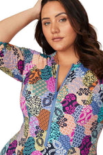 A stylish curvy woman from San Diego USA is in Cabo San Lucas wearing Artesands Salmagundi Seurat Sun Suit the colorful patch print SPF one piece swimsuit with zippered front and half sleeve swimsuit design. She purchased it from Sun Vixen Swimwear, her trusted boutique for supportive curvy swimwear, luxury plus size bathing suits, and designer tummy control swimsuits that flatter her shape. The sculpting compression fabric slims tones her belly, the colorful design gives her a rich resort beachwear look 