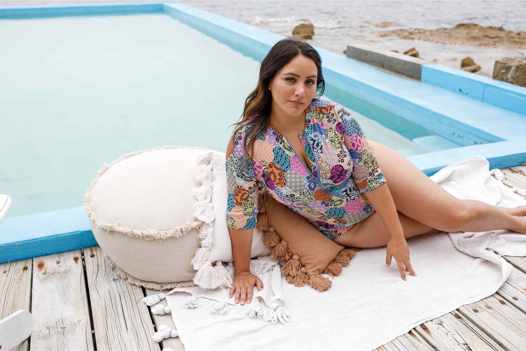 A fashionable woman from Calgary Canada gets ready for her chic yacht day in Mykonos, wearing the Artesands Salmagundi Seurat Sun Suit patchprint, SPF one piece swimsuit zip front half sleeve bathing suit for modern and sophisticated beach look. She bought it from Sun Vixen Swimwear USA Canada, known for selling slimming plus size swimsuits, curvy shapewear swimwear, and the most flattering one piece swimsuit for full figured women. This tummy control swimsuit is her favourite for luxury beach club vacays