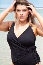 A stylish plus size woman from Toronto Canada packs her Tummy Control Black Hayes Underwire One Piece Swimsuit for a winter getaway and tries it on in her hotel room feeling instantly shaped and lifted. The wrap tummy control swimsuit gives her a slimming secure fit while the designer detailing brings a luxury touch to her swimwear wardrobe. She prefers high quality elegant swimsuits, sophisticated swimwear for curvy women that feel flattering and timeless, and this black one piece swimsuit fits her needs