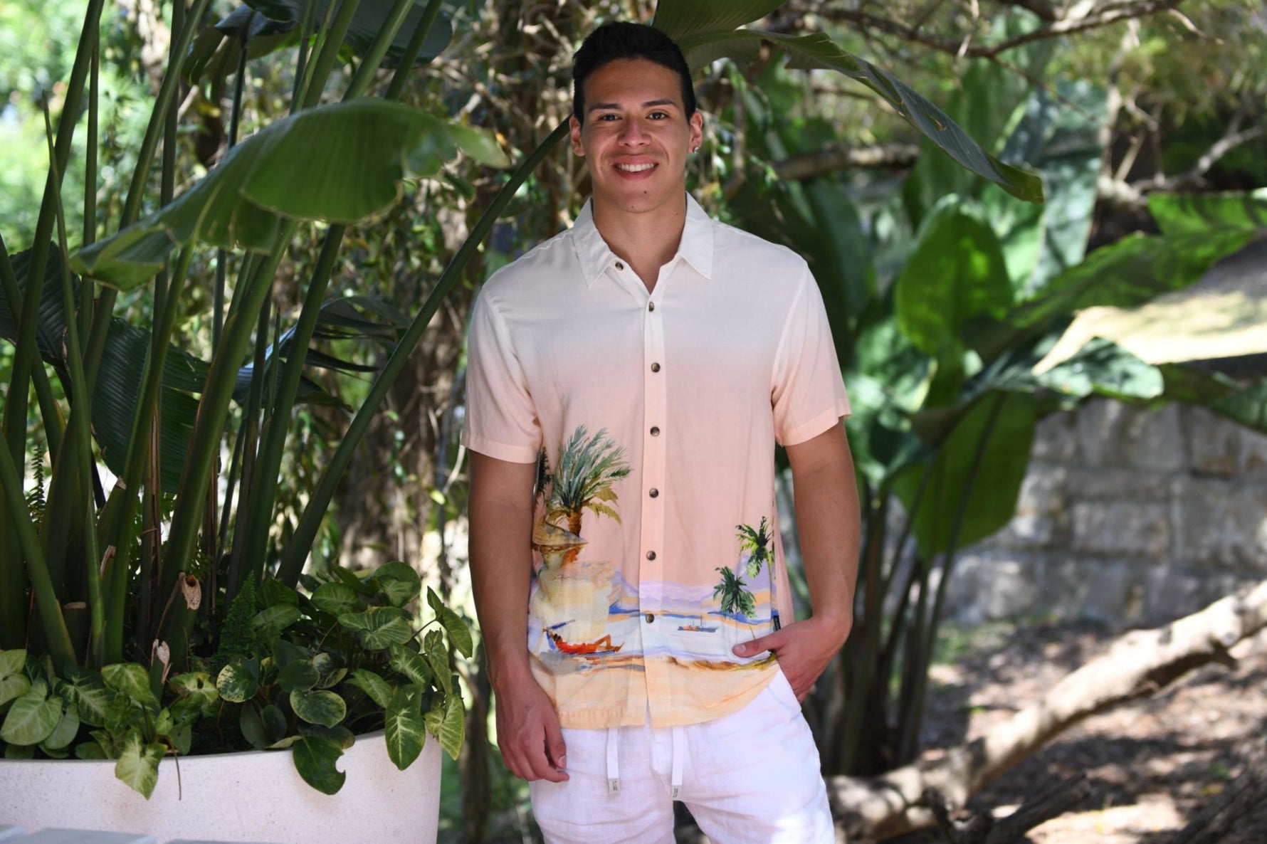 A stylish man wears a designer Hawaiian beach shirt from Sun Vixen Swimwear on a tropical vacation. This mens designer swimwear store offers the best luxury beach shirts, featuring floral beach shirts, designer mens beachwear, and premium resort shirts, perfect for a smart resort  beach look. This mens designer swimwear store features the best luxury beach shirts, cool beach shirts, sustainable mens beachwear, and tropical shirts, stylish resort shirts, and stylish resort shirts, high end designer beachw