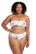 A plus size woman from Winnipeg Canada is enjoying her sunny holiday in the White Vermeer Clementine flounce bikini by Artesands, loving the floral ruffles, sculpting tummy control, and shaping compression high waist bikini bottoms. She wants most flattering bikinis for plus size women online and always shops at Sun Vixen Swimwear for sexy plus swimsuits made for curvy bodies. She loves how the floral print makes her look elegant. The supportive top keeps her comfortable on her luxury resort vacation Bali