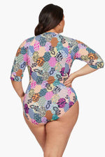 A plus size woman from Edmonton Canada travels to the Maldives for a luxury holiday wears Salmagundi Seurat Sun Suit colorful designer one piece swimsuit Artesands SPF, supportive half sleeve zip front one piece swimsuit that gives her a sculpted, slimmed look. She bought it online from Sun Vixen Swimwear USA Canada, known for carrying the most flattering swimsuits for plus size women, sexy slimming resort swimwear, and premium tummy control suits. She loves how the supportive swimsuit hides her belly pooch