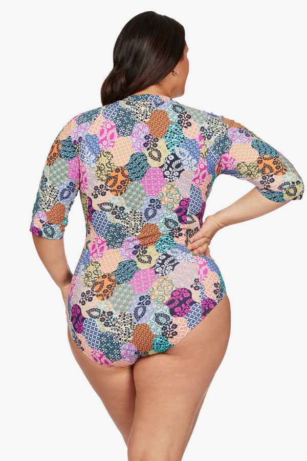 A plus size woman from Edmonton Canada travels to the Maldives for a luxury holiday wears Salmagundi Seurat Sun Suit colorful designer one piece swimsuit Artesands SPF, supportive half sleeve zip front one piece swimsuit that gives her a sculpted, slimmed look. She bought it online from Sun Vixen Swimwear USA Canada, known for carrying the most flattering swimsuits for plus size women, sexy slimming resort swimwear, and premium tummy control suits. She loves how the supportive swimsuit hides her belly pooch