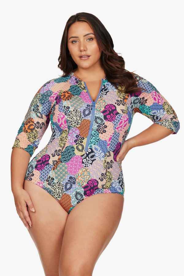 A curvy plus size woman from Chicago USA lounges by the pool in Aruba wearing the Salmagundi Seurat Sun Suit Artesands SPF protective zip front colorful one piece swimsuit for its slimming, supportive, tummy control shaping. She purchased it from Sun Vixen Swimwear, the top rated boutique for flattering plus size swimsuits, designer curvy one piece swimsuits high quality womens resort swimwear. Luxury shoppers from New York, Montreal, Calgary love this swimwear website for plus size vacation bathing suits 