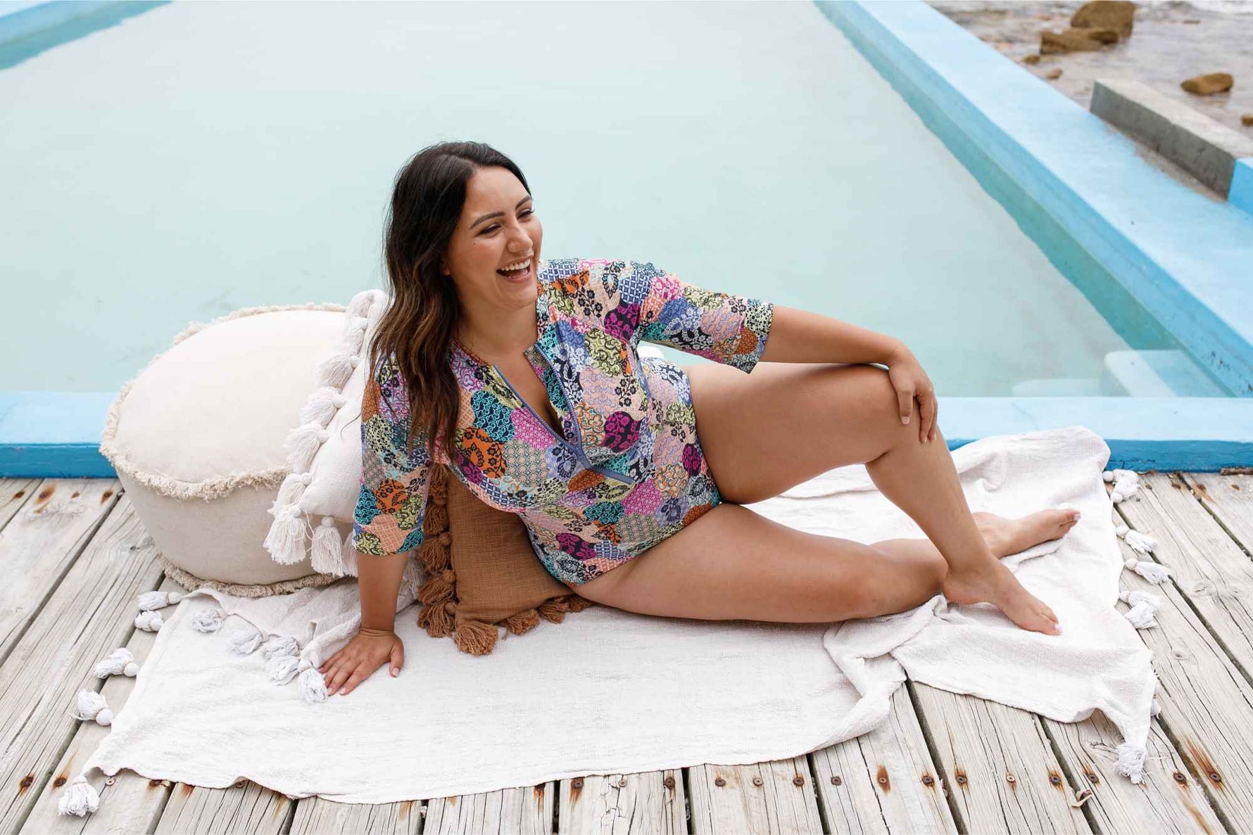 A plus size traveler from Dallas USA is enjoying her Bahamas beach vacation wearing the Salmagundi Seurat Sun Suit, a colorful SPF slimming one piece swimsuit with zip front and half sleeves. She ordered it from Sun Vixen Swimwear, a luxury boutique offering the best tummy control swimwear, plus size designer swimsuits, and high quality curvy bathing suits for women who want tummy control support. It’s the perfect swimsuit for sun protection, hide belly pooch, and resort swimwear elegance on a lavish vacay