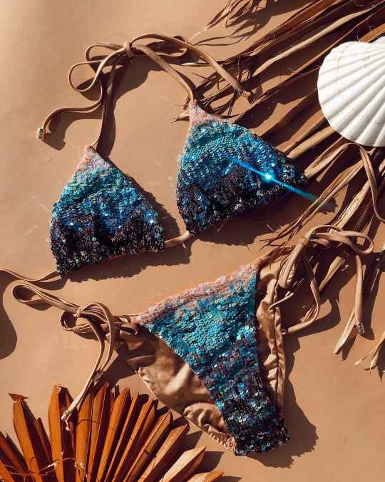 woman wearing glamorous Beach bunny swimwear ariel ombre sequin bikini ideal for high end holiday resorts featuring its shimmering glitter sparkle shiny embellished sliding triangle top with opulent top notch sequin accents in mermaid ombre deep teal and bold sparkling turquoise, matched with skimpy side tie bikini bottoms with itsy bitsy cheeky coverage and adjustable tie sides for a tailored fit perfect for the hottest provocative designer beach styles that draw attention at luxurious poolside resort trip