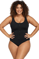 Confident curvy woman in Chicago USA is relaxing in the spa lounge wearing the Artesands Natare Black Chlorine Resistant Fuseli Zip One Piece, a luxury plus size swimsuit known for its shaping and best tummy control fit. She’s shopping for her girls trip to Maldives, and she wanted a sexy but classy designer one piece swimsuit that looks beautifully on high end beach vacations. She ordered it from Sun Vixen Swimwear, the boutique she trusts for high quality slimming swimwear that slims tones belly pooch